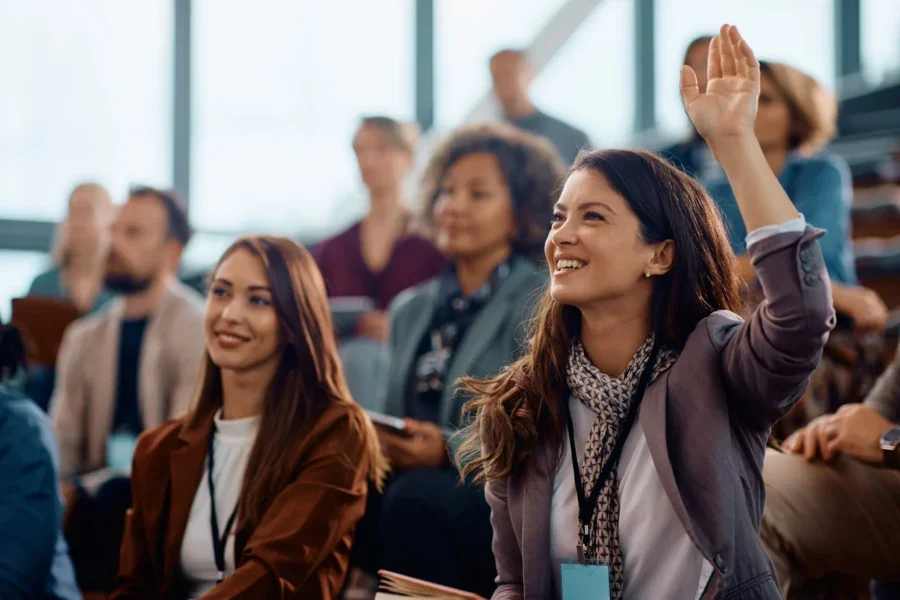 Happy businesswoman raising hand to ask a question attending a seminar in conference hall.