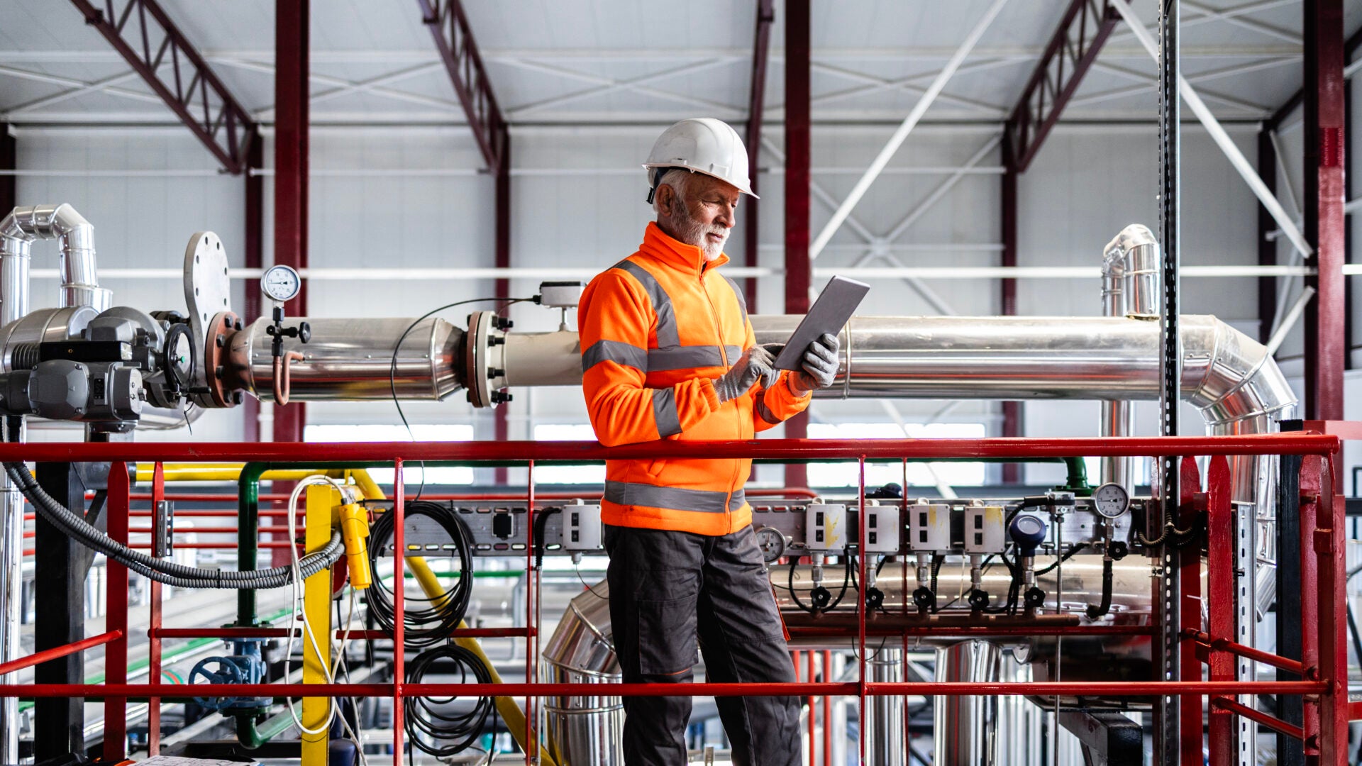 Engineer wearing hard hat and safety vest checking equipment in a factory setting