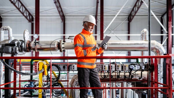 Engineer wearing hard hat and safety vest checking equipment in a factory setting