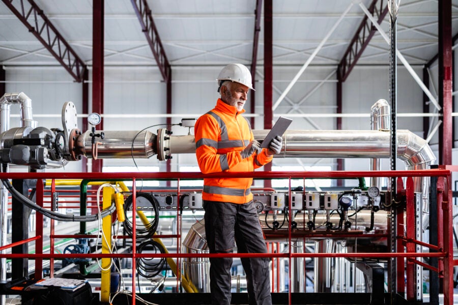Engineer wearing hard hat and safety vest checking equipment in a factory setting