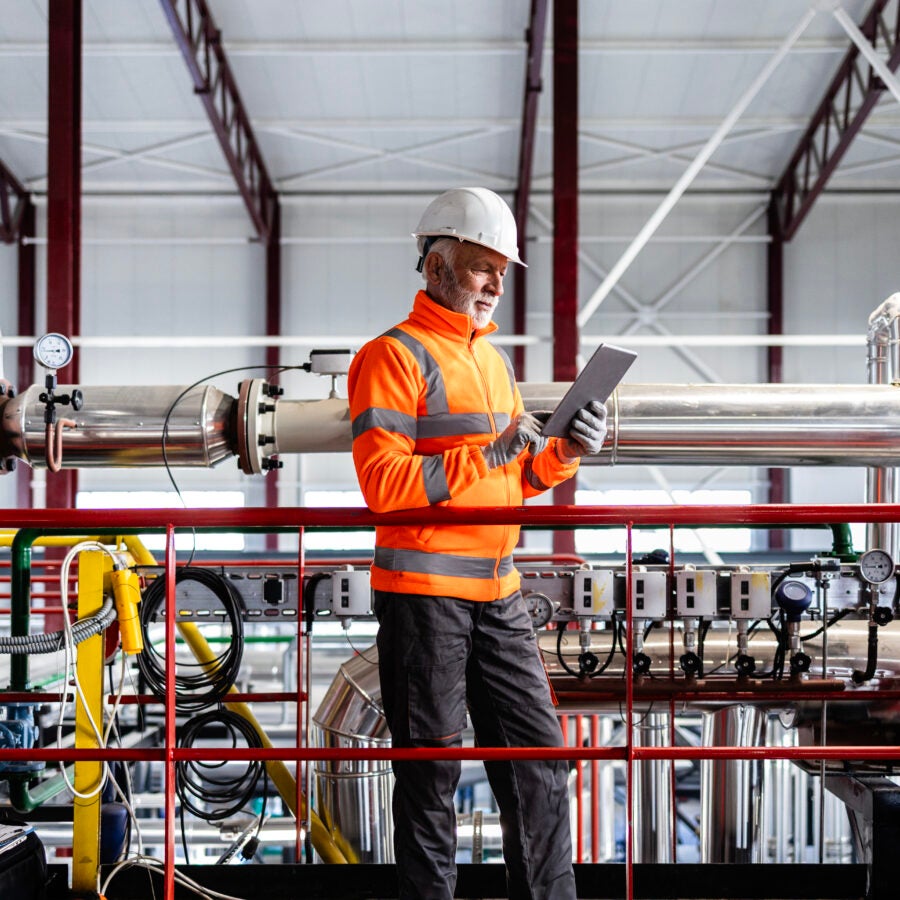 Engineer wearing hard hat and safety vest checking equipment in a factory setting