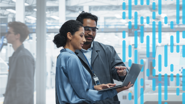 A manager and an engineer review information on a laptop together on a manufacturing facility floor.