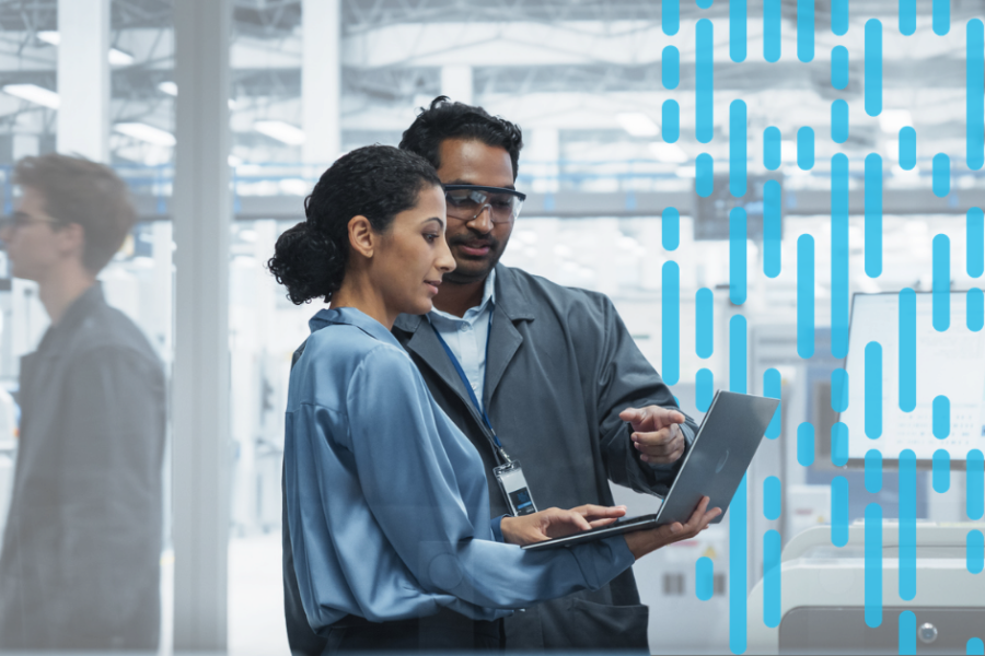 A manager and an engineer review information on a laptop together on a manufacturing facility floor.