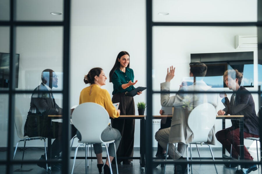 Diverse group of business professionals discussing ideas and strategy during a modern office meeting. Corporate teamwork, communication, innovation, leadership, and collaboration in a contemporary workplace environment with natural light and technology